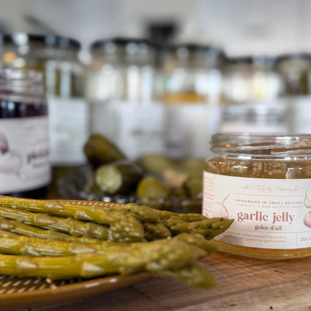 Jar of garlic jelly with asparagus on a wooden surface, with blurred jars in the background.