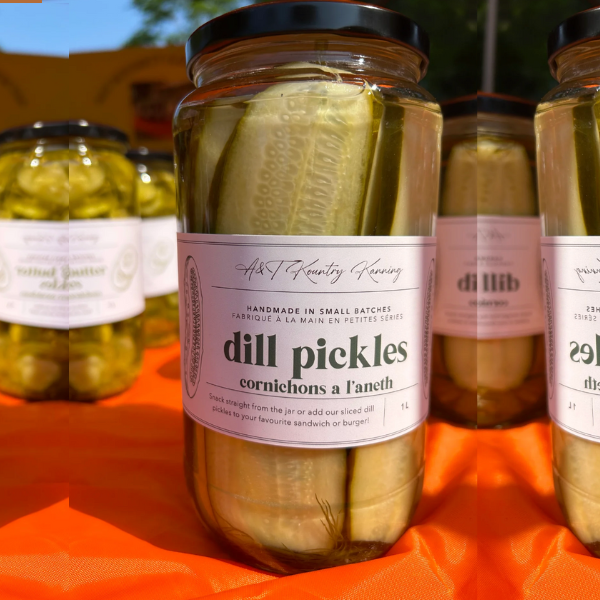 Jars of Dill Pickles on a table with a label that reads 'A&T Kountry Kanning, Dill Pickles, Small Batch, Handcrafted, Since 2007'.