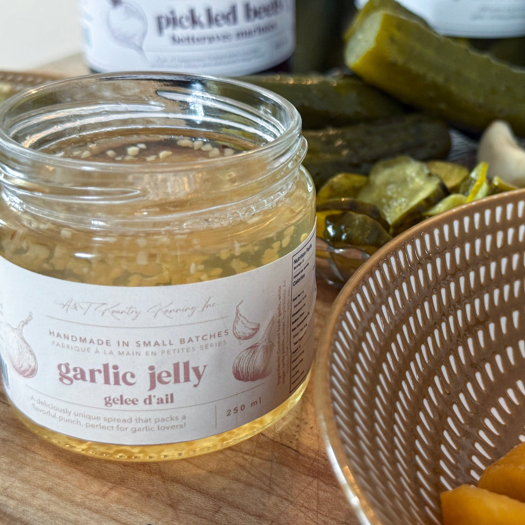 Jar of garlic jelly with pickles and bread in the background.