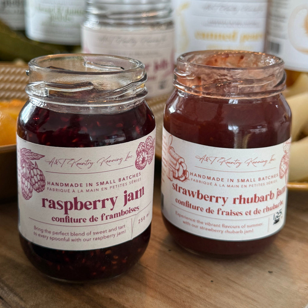 Two jars of raspberry and strawberry rhubarb jam on a wooden surface with more jars in the background.